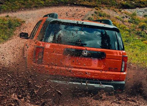 An orange 2026 Passport TrailSport rides the off-road, spraying mud over its body