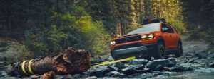 An orange 2026 Passport Trailsport pulls a fallen branch out of its way on the rocky forest offroad