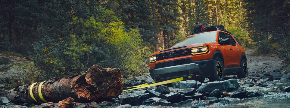 An orange 2026 Passport Trailsport pulls a fallen branch out of its way on the rocky forest offroad